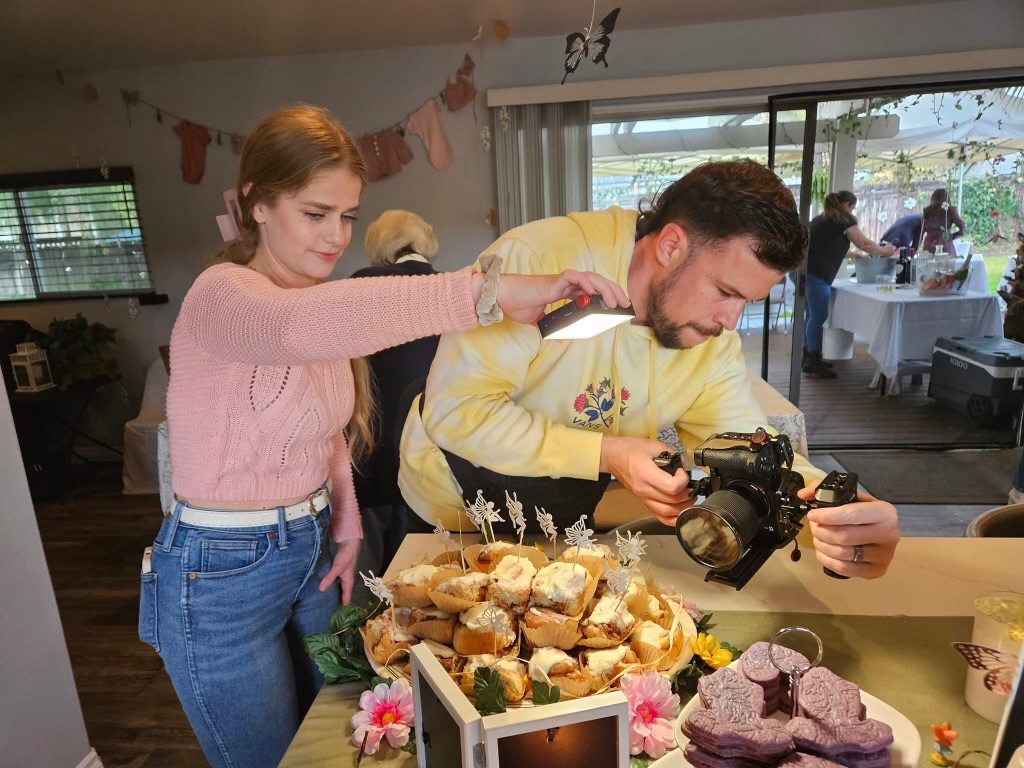 Erick filming a dessert table while Sammie holds a light